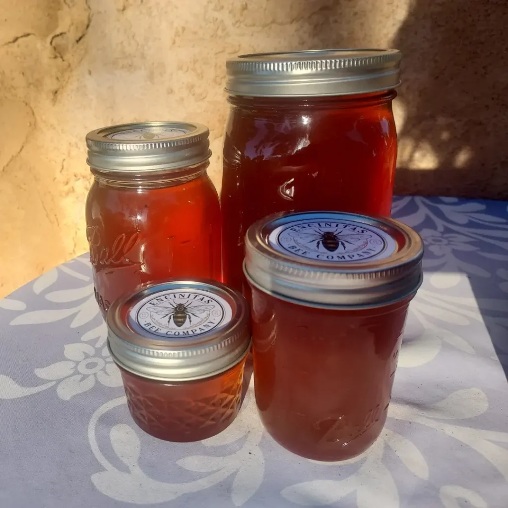 Four jars of honey in varying sizes on a table.